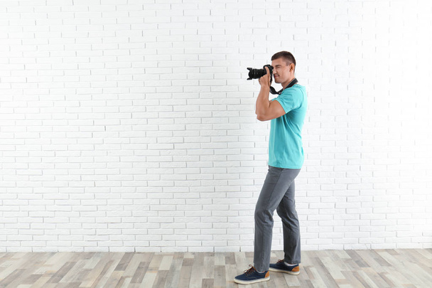 Young professional photographer taking picture near brick wall. Space for text - Fotografie, Obrázek