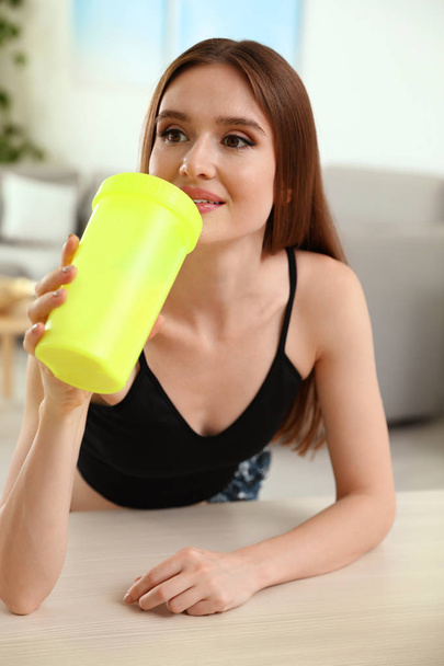 Young woman drinking protein shake at table indoors - Valokuva, kuva