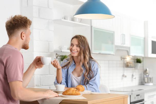 Happy young couple having breakfast at table in kitchen - Fotoğraf, Görsel