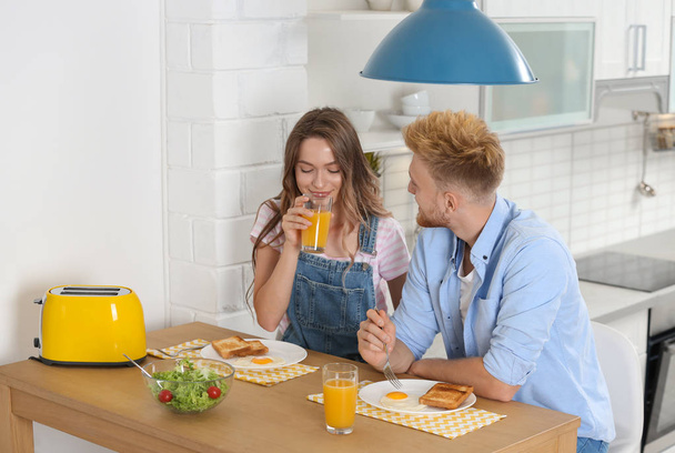 Happy young couple having breakfast at table in kitchen - Foto, afbeelding