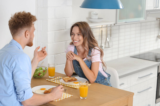 Happy young couple having breakfast at table in kitchen - Φωτογραφία, εικόνα