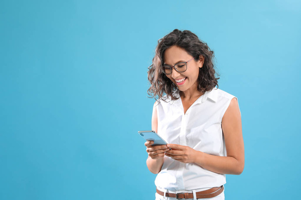Happy young woman using smartphone on blue background. Space for text - Φωτογραφία, εικόνα