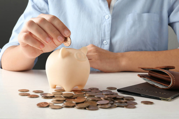 Young woman putting coin into piggy bank at wooden table, closeup view - Foto, Imagem