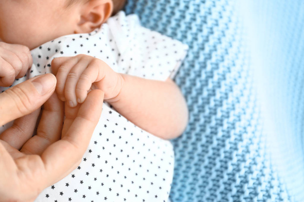 Cute little baby holding mother's hand on light blue plaid, closeup. Space for text - Zdjęcie, obraz