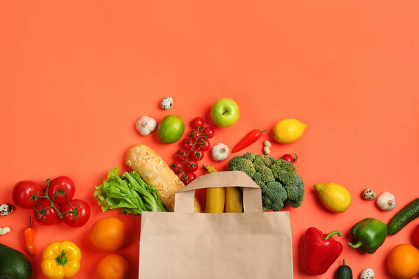 Paper bag with different groceries on coral background, flat lay - Fotoğraf, Görsel