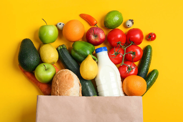 Paper bag with different groceries on yellow background, flat lay - Φωτογραφία, εικόνα