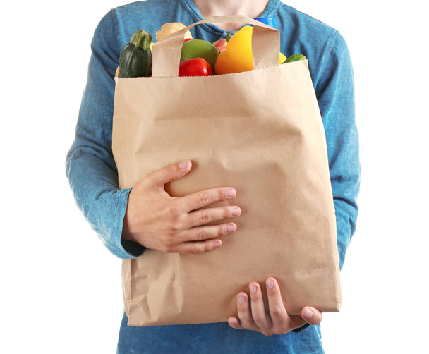 Man holding paper bag with different groceries on white background, closeup view - Фото, изображение