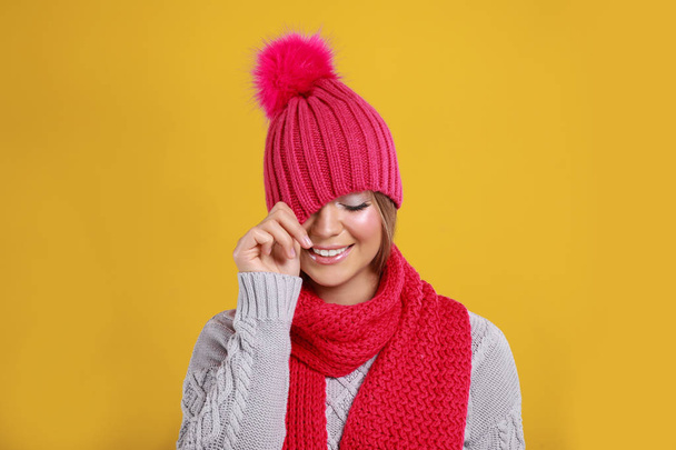 Funny young woman in warm sweater, scarf and hat on yellow background. Winter season - Foto, imagen