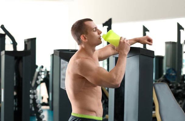Αθλητικός νέος άνθρωπος πίνοντας πρωτεΐνη μιλκσέικ στο γυμναστήριο - Φωτογραφία, εικόνα