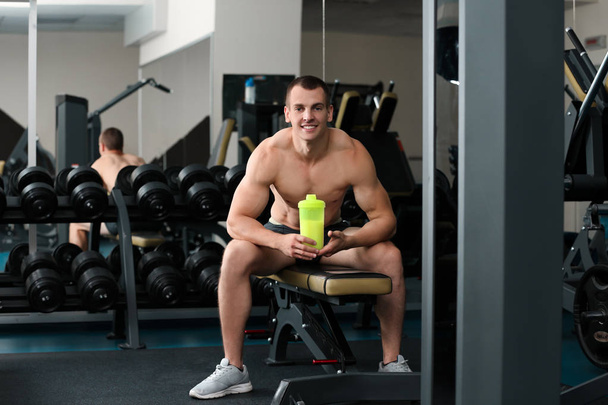 Athletic young man with protein shake in gym - Фото, зображення