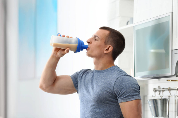 Athletic young man drinking protein shake in kitchen - Photo, image