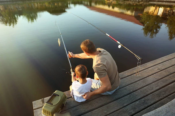 Dad and son fishing together on sunny day - 写真・画像