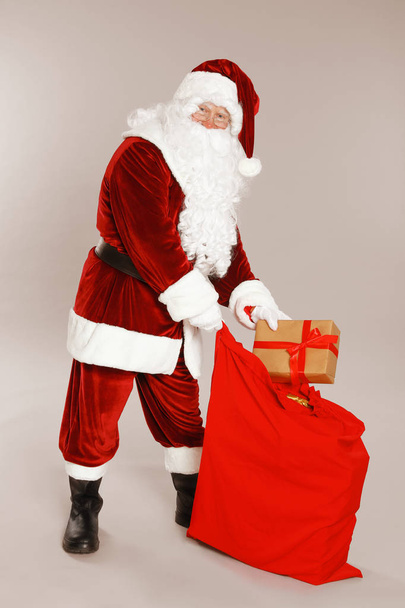 Authentic Santa Claus with sack and gift on grey background - Zdjęcie, obraz