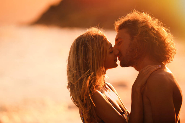 Young woman in bikini kissing her boyfriend on beach at sunset. Lovely couple - Foto, Imagem
