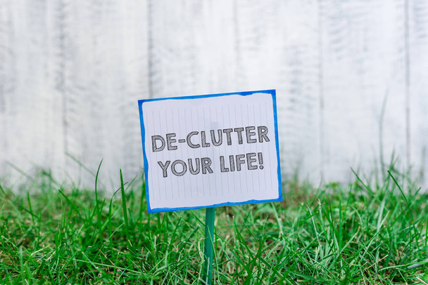 Handwriting text De Clutter Your Life. Concept meaning remove unnecessary items from untidy or overcrowded places Plain empty paper attached to a stick and placed in the green grassy land. - Photo, Image