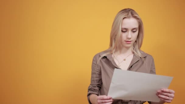 blond meisje in bruine blouse over geïsoleerde oranje achtergrond toont emoties - Video