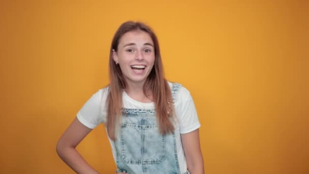 Jovem mulher vestindo camiseta branca, sobre fundo laranja mostra emoções
 - Filmagem, Vídeo