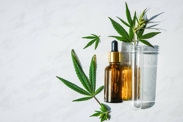 Glazen fles met cannabisolie en een reageerbuis met hennep bladeren op een marmeren achtergrond. Ruimte kopiëren. - Foto, afbeelding