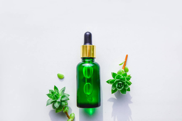 Suero natural de extractos en una botella de vidrio verde con una pipeta. Suculentas, fondo blanco
. - Foto, Imagen