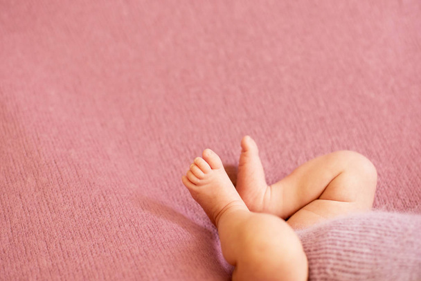  Füße des neugeborenen Mädchens mit rosa Blüten, Finger am Fuß, mütterliche Pflege, Liebe und Umarmungen in der Familie, Zärtlichkeit.  - Foto, Bild