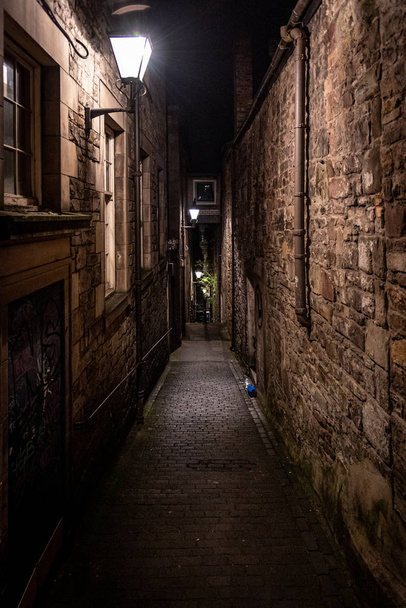 A dark creepy narrow European alley at night, surrounded by bricks and cobblestone. Illuminated only with some street lamps. Concept of scared or being alone and frightened - Zdjęcie, obraz