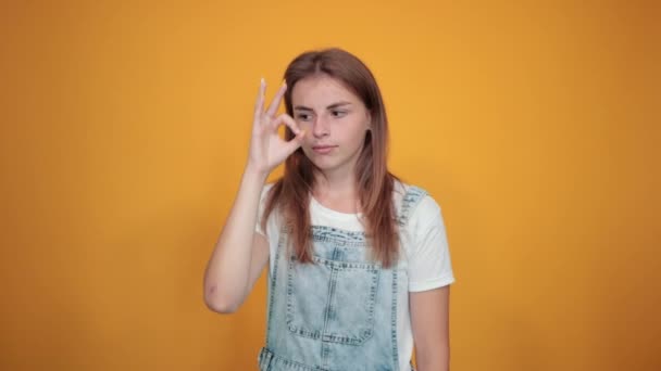 Mujer joven vistiendo camiseta blanca, sobre fondo naranja muestra emociones
 - Metraje, vídeo