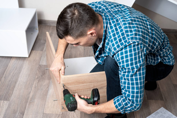 Top view joven hombre caucásico se dedica a ensamblar muebles con un destornillador eléctrico
 - Foto, imagen