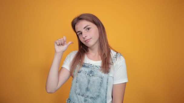 Young woman wearing white t-shirt, over orange background shows emotions - Кадры, видео