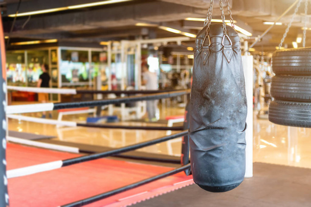 Black punching bag hanging in Abstract blur of defocused boxing gym interior and fitness health club with sports exercise equipment Gym blur background. - Foto, Imagem