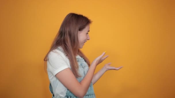 Młoda kobieta ubrana w białą koszulkę, na pomarańczowym tle pokazuje emocje - Materiał filmowy, wideo