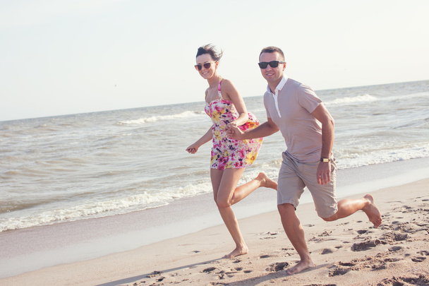 Happy couple in sunglasses. Run on the beach holding hands. Dynamic shot outdoors - Photo, Image
