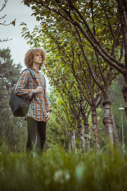 curly-haired young guy stands on the street with a satchel on his shoulder. student and young traveler concept. portrait of a young man - Valokuva, kuva