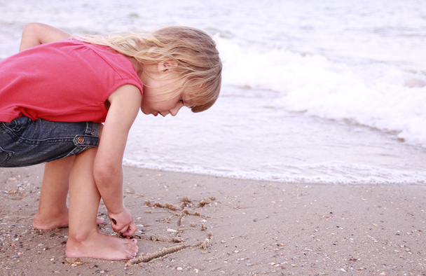 Little girl draws a sun in the sand on the beach - Valokuva, kuva