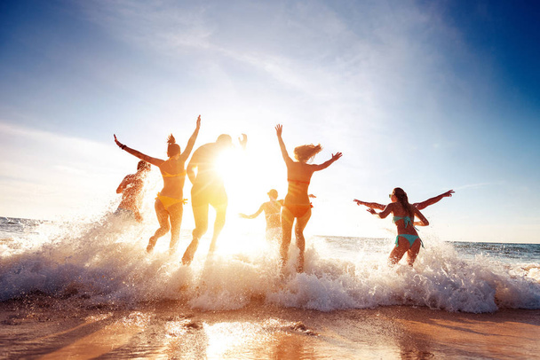 Big group happy friends runs and having fun at sunset beach - 写真・画像
