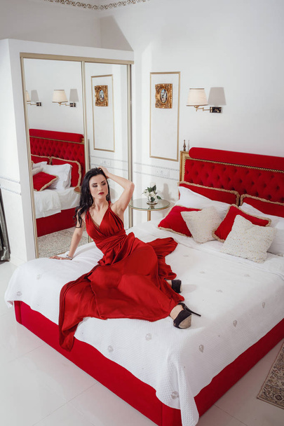 csábító pihentető egy kanapén, luxus belső piros ruhás nő - Fotó, kép