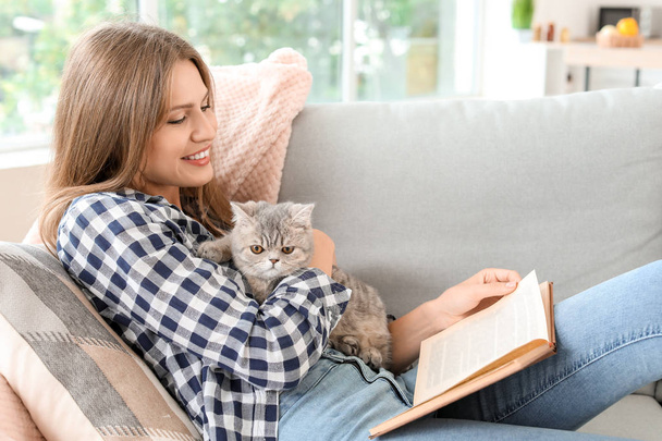Schöne junge Frau mit niedlichem Katzenlesebuch zu Hause - Foto, Bild
