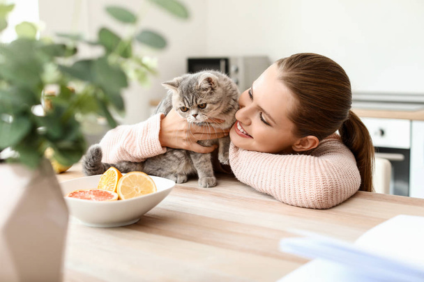 Mooie jonge vrouw met schattige kat in keuken - Foto, afbeelding
