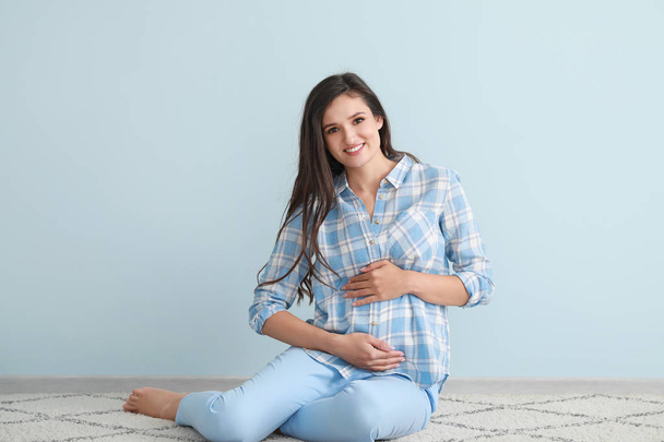 Молода вагітна жінка сидить на підлозі біля кольорової стіни
 - Фото, зображення