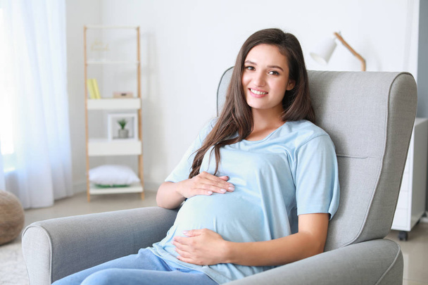 Młoda kobieta w ciąży, siedząc w fotelu w domu - Zdjęcie, obraz