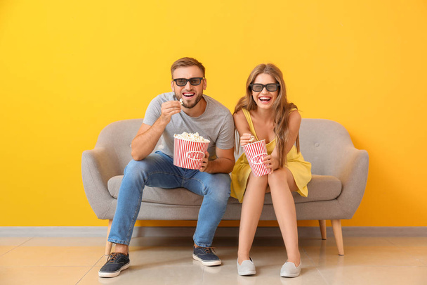 Νεαρό ζευγάρι με ποπκόρν βλέποντας ταινία στον καναπέ κοντά στο χρώμα τοίχου - Φωτογραφία, εικόνα