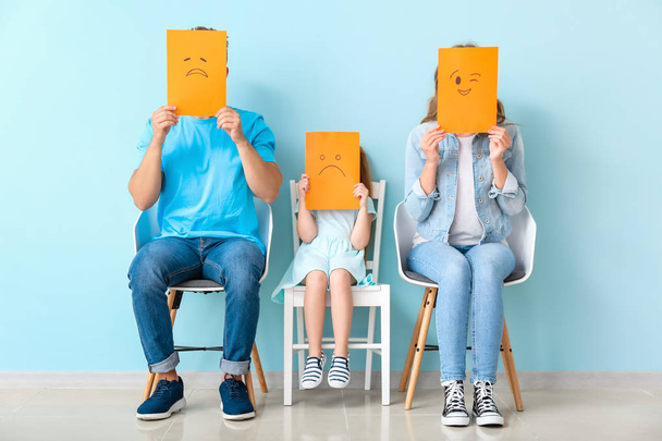 Young family hiding faces behind emoticons near color wall - Photo, Image