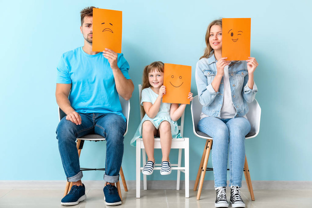 Young family with emoticons sitting on chairs near color wall - Foto, Imagen