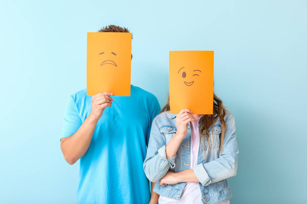 Young couple hiding faces behind emoticons against color background - Photo, Image