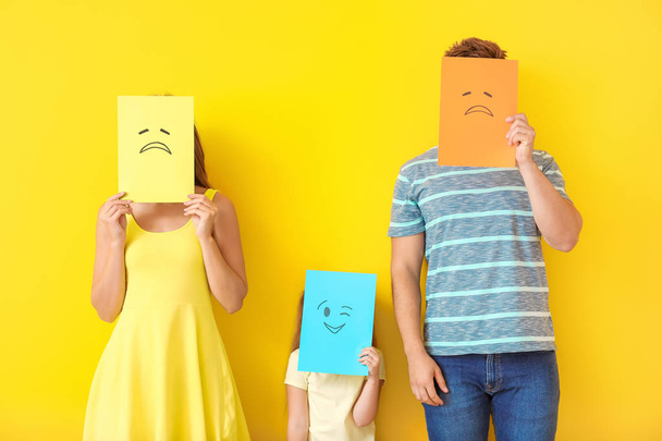 Family hiding faces behind emoticons against color background - Фото, изображение