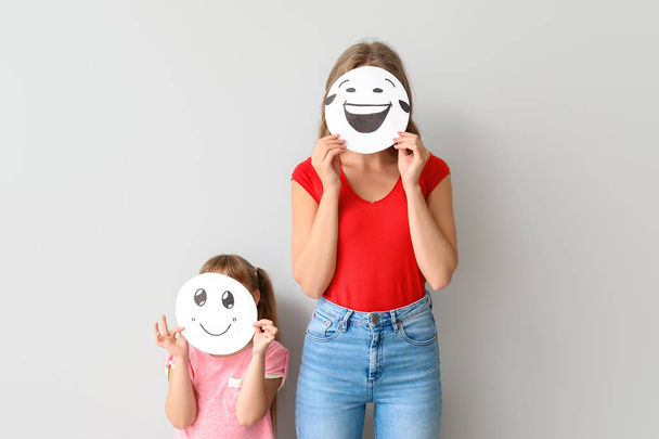 Mutter und kleine Tochter verstecken Gesichter hinter Emoticons vor hellem Hintergrund - Foto, Bild
