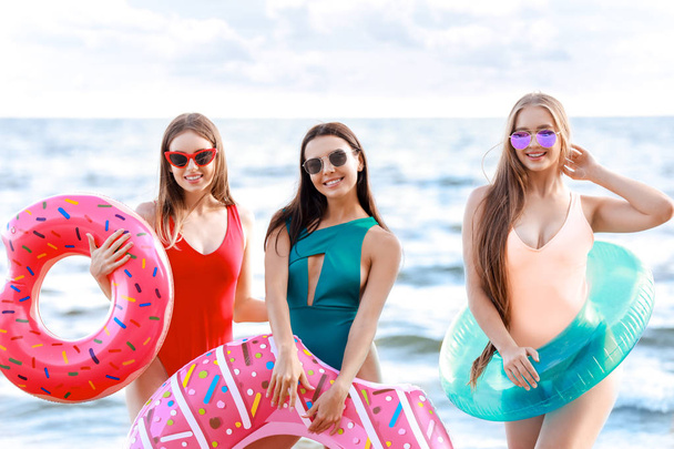 Hermosas mujeres jóvenes con anillos de natación en la playa del mar en el complejo
 - Foto, Imagen