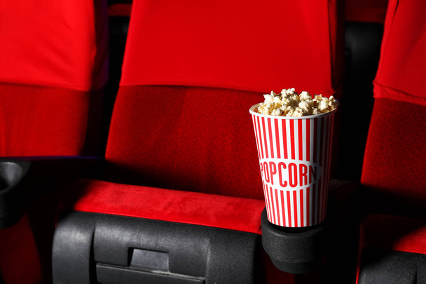 Cup of popcorn on chair in empty cinema - 写真・画像