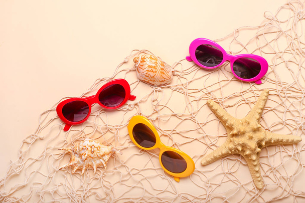 Diferentes óculos de sol elegantes com rede e conchas no fundo claro
 - Foto, Imagem