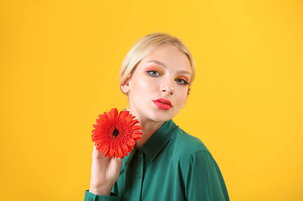 色の背景にガーベラの花を持つ美しい若い女性 - 写真・画像