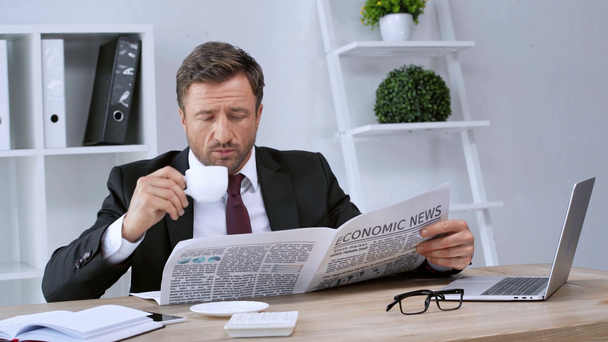 成熟したビジネスマンが経済新聞を読み、オフィスでコーヒーを飲む - 映像、動画